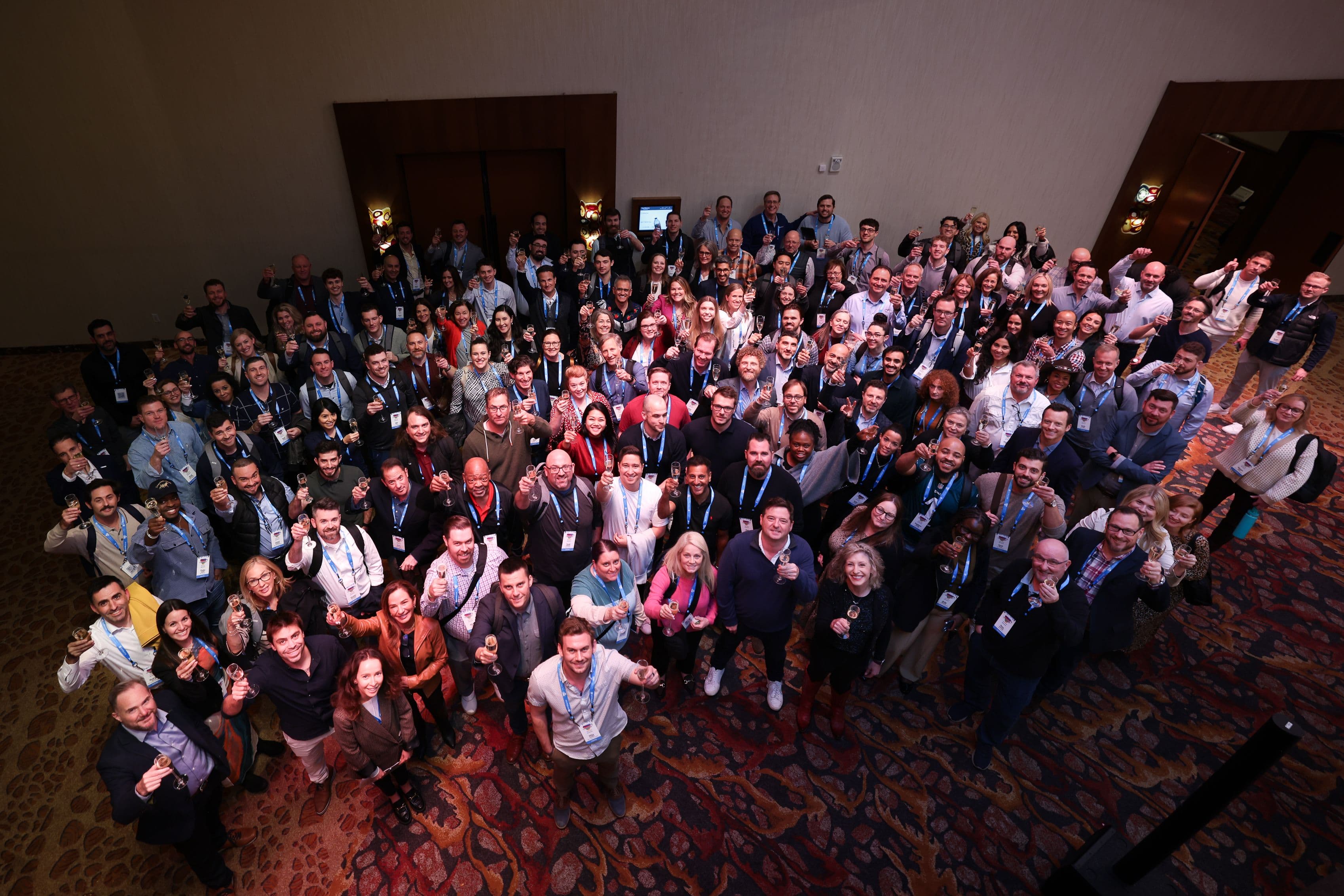 A large group of smiling people giving thumbs up at a conference.