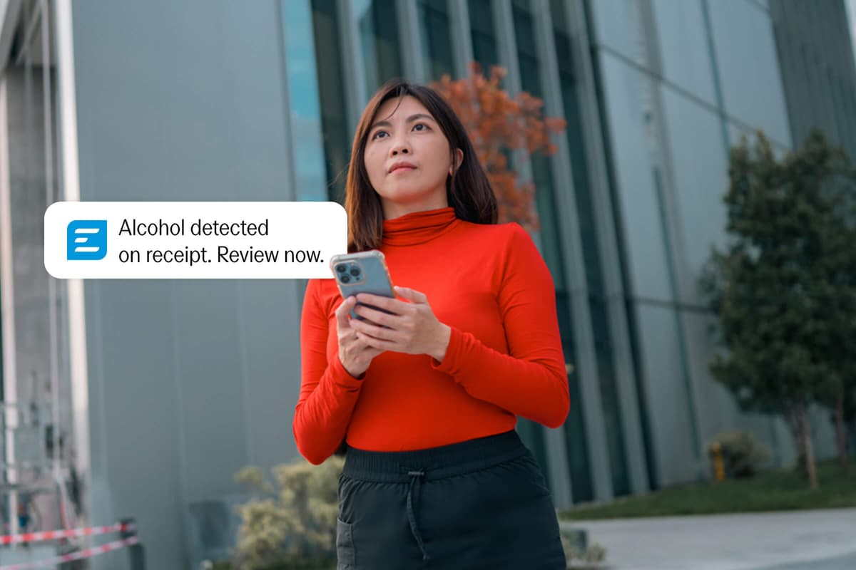 A woman holds a smartphone, with a notification bubble reading "Alcohol detected on receipt. Review now."